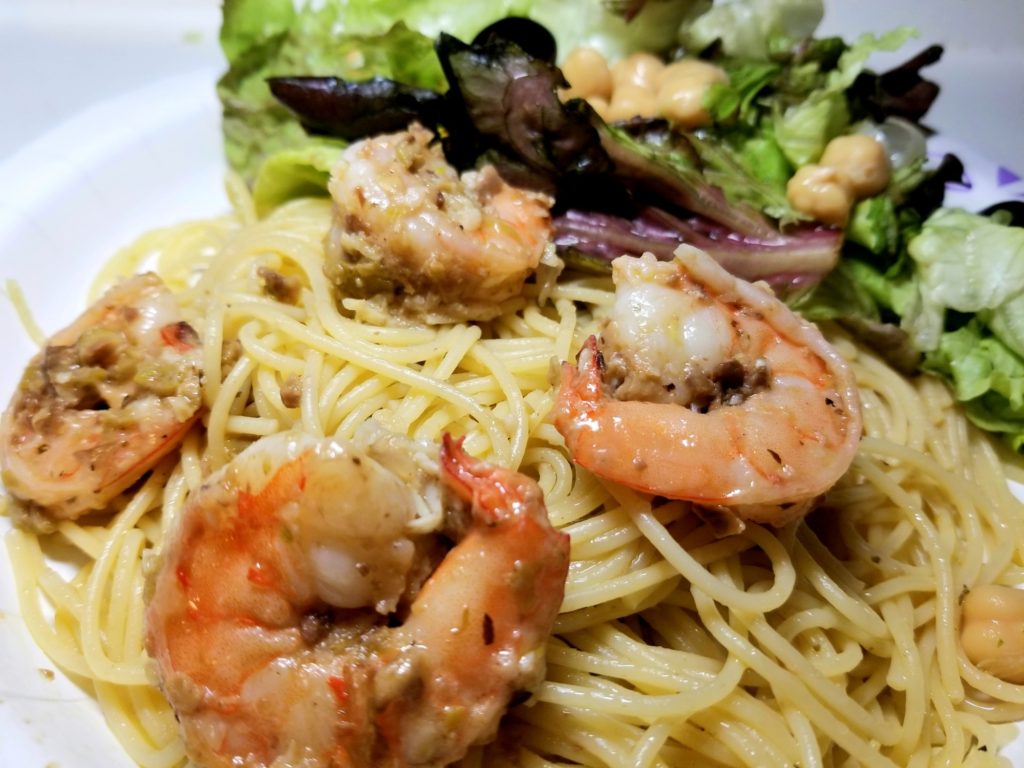 Tapenade and Shrimp tossed with pasta on a paper plate.